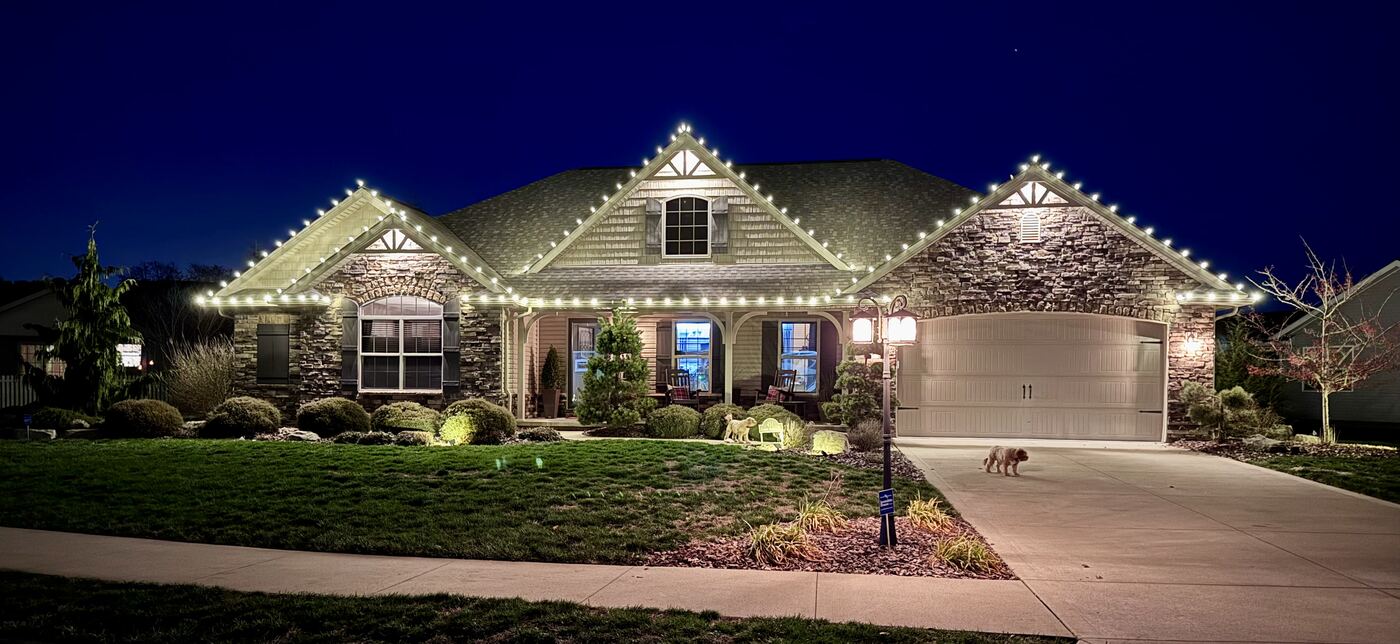 Warm white holiday roofline lighting on a stone and shake craftsman home at dusk